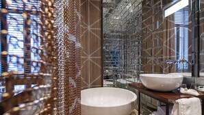 Een moderne badkamer met een ruim vrijstaand bad, een wastafel met spiegel en uitzicht op de stad door grote ramen.