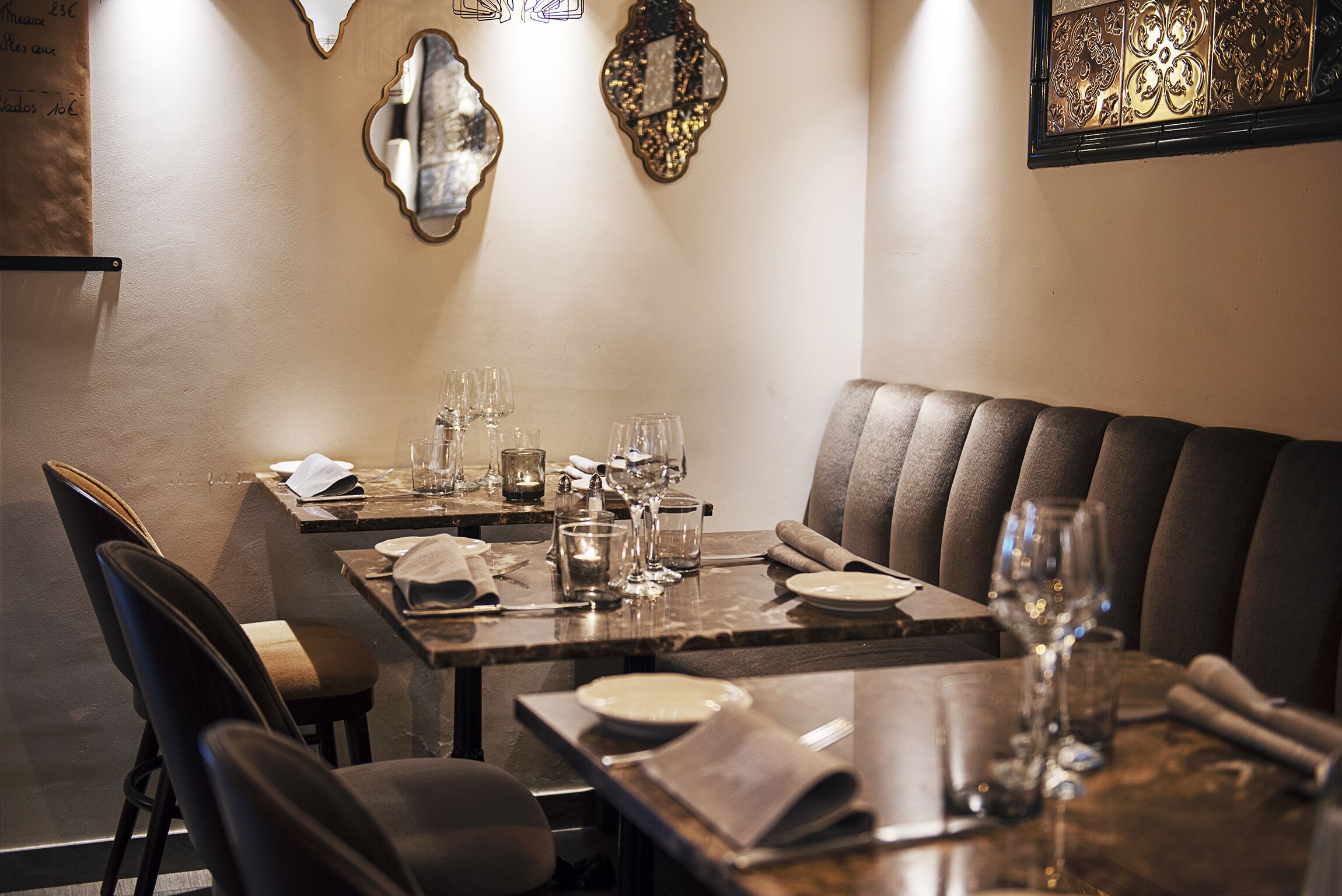 A dining area with a booth and a table set for two, featuring a candle, wine glasses, and a menu.
