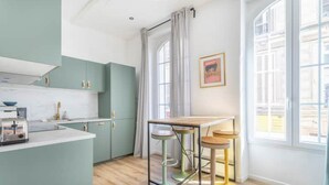 A modern kitchen with teal cabinets, a wooden countertop, and a dining area with stools. - Cosy Appartement au Coeur du Cours Julien (Marseille)