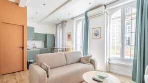 A living room with a sofa, a coffee table, and a view of a cityscape through large windows. - Cosy Appartement au Coeur du Cours Julien (Marseille)