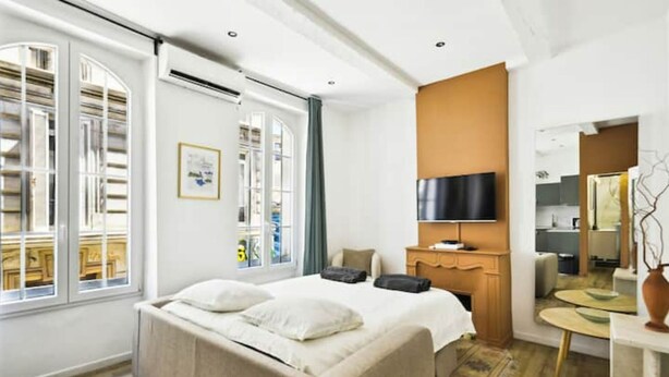 A modern hotel room with a large bed, a flat-screen TV, a wooden dresser, and a small round table. - Cosy Appartement au Coeur du Cours Julien (Marseille)