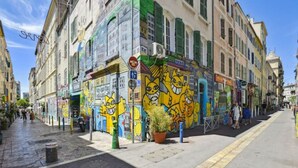 A street with colorful murals on a building, a clear sky, and a pedestrian walkway. - Cosy Appartement au Coeur du Cours Julien (Marseille)