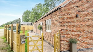 A brick building with a wooden gate, a paved patio, and a small garden area. - 2 bedroom accommodation in Sloothby (Sloothby)