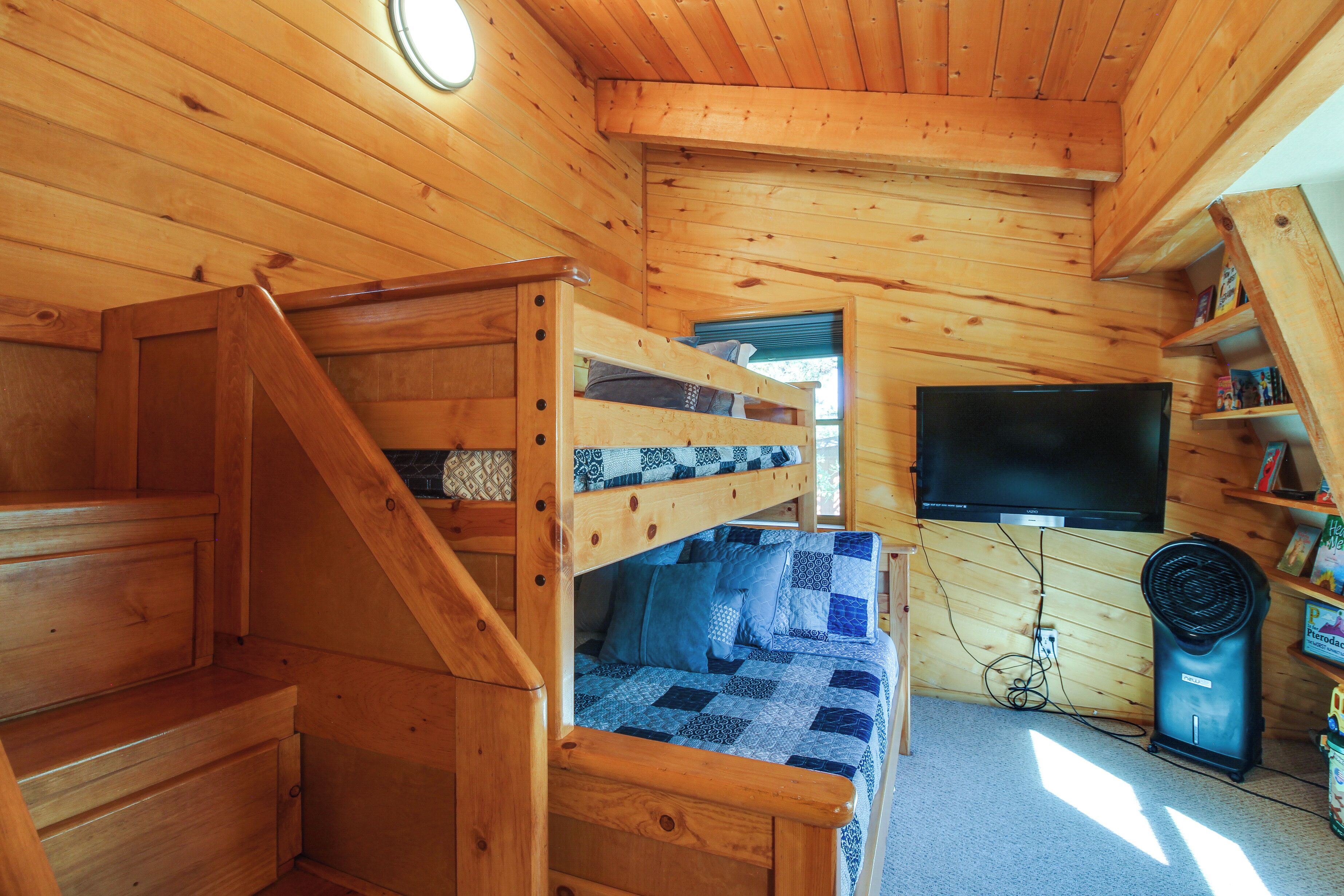 A wooden cabin interior with a bunk bed, a flat-screen TV, and a fan.