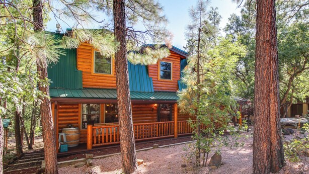 A log cabin with a green roof, surrounded by trees and gravel. - Hot Tub + Decks: Sherwood Forest Cabin (Lakeside)
