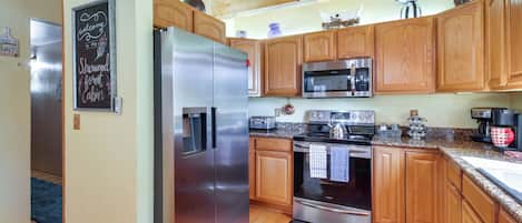 A modern kitchen with wooden cabinets, stainless steel appliances, and a chalkboard sign.