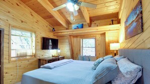A wooden cabin bedroom with a bed, pillows, a desk, and a television. - Hot Tub + Decks: Sherwood Forest Cabin (Lakeside)