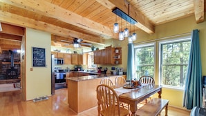 A spacious kitchen with wooden cabinets, a central island, and a dining area with wooden chairs and a table. - Hot Tub + Decks: Sherwood Forest Cabin (Lakeside)