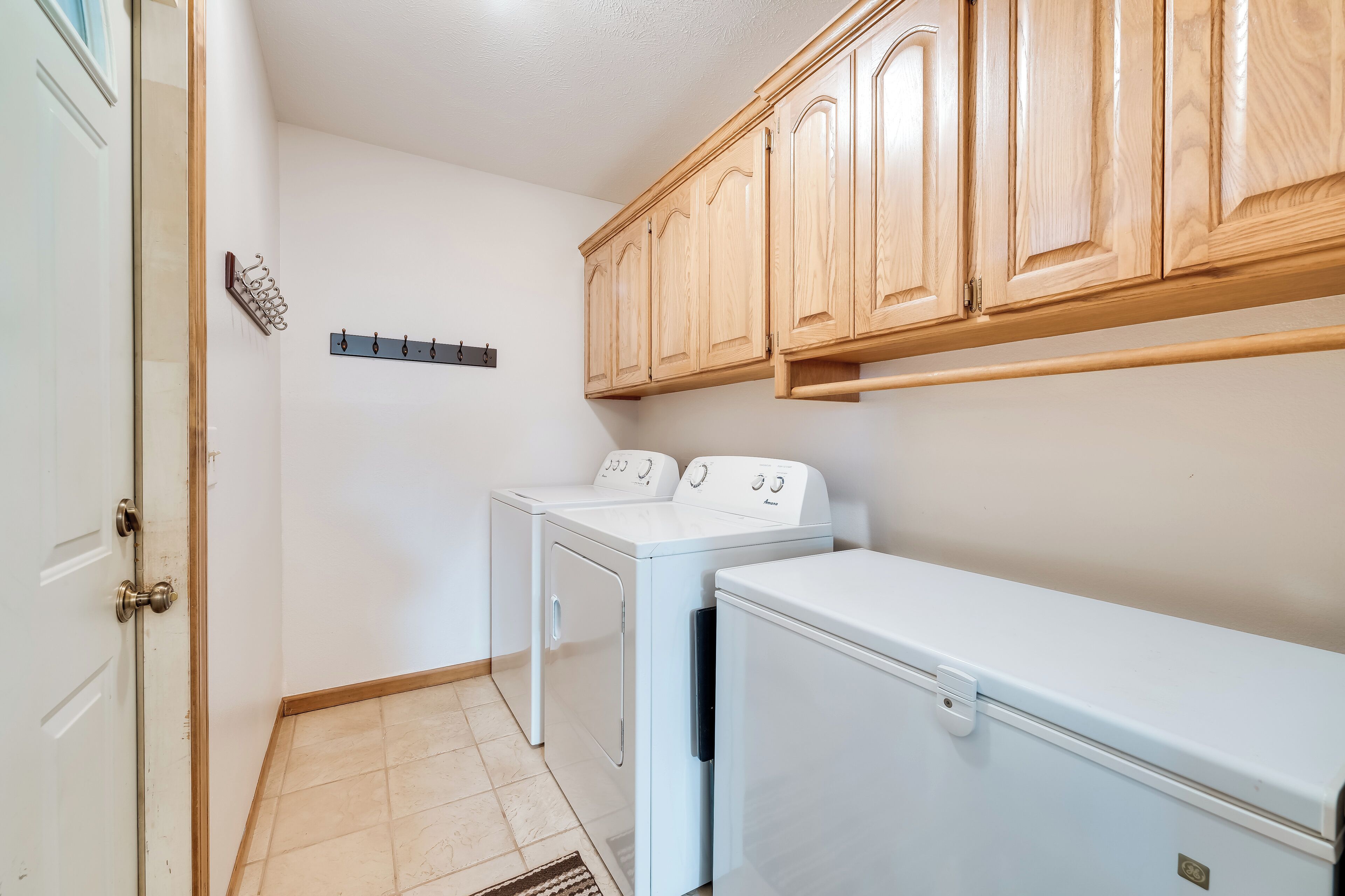 A laundry room with two washing machines, wooden cabinets, and a metal coat rack.