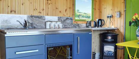 Cocina compacta con paredes de madera, horno empotrado, estufa y ventana con vistas a la vegetación.