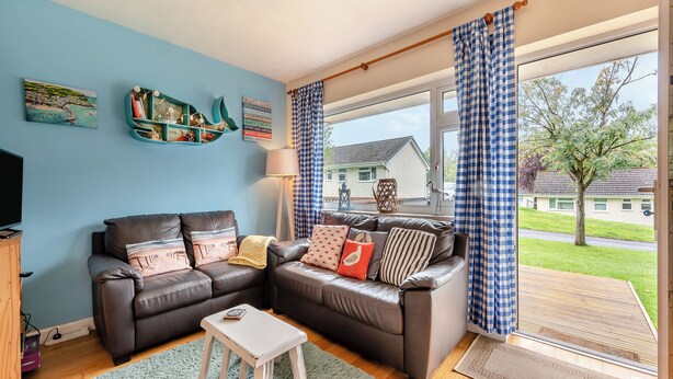 Een woonkamer met een bruine leren bank, een witte salontafel en een blauw-witte geruite gordijn.