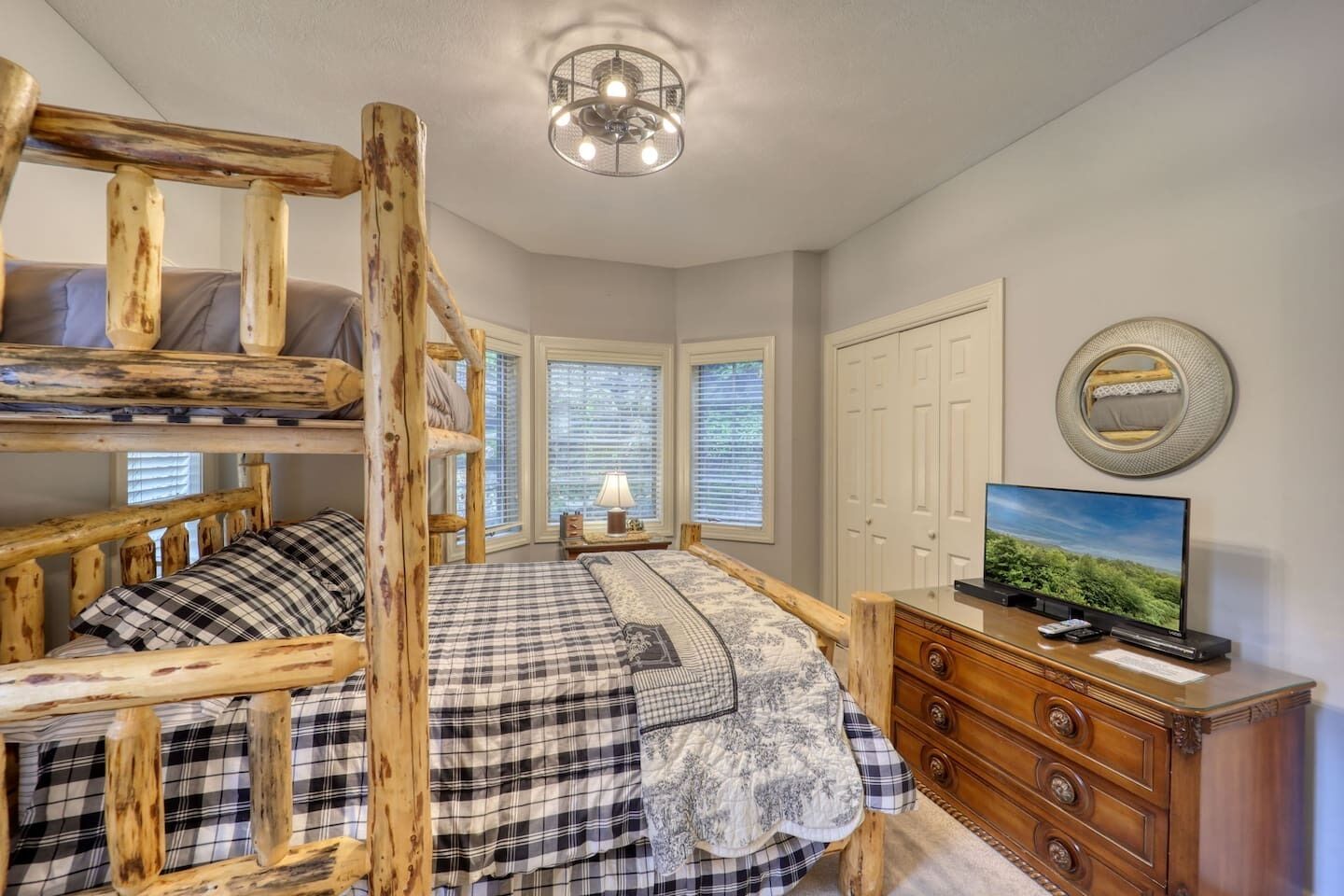 A bedroom with a bunk bed, a dresser, a television, and a chandelier.