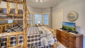 Ein Schlafzimmer mit Etagenbett, Kommode, Fernseher und einer Chandelier.