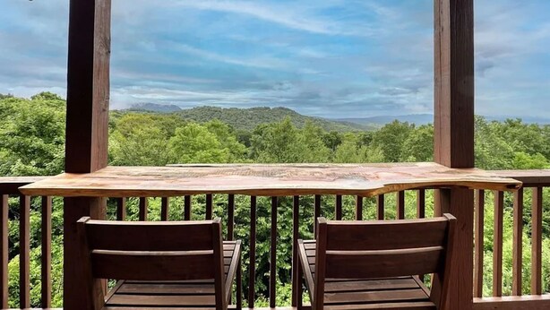 Eine Holzdar Terrasse mit zwei Stühlen und einem Tisch, mit Blick auf eine bewaldete Landschaft mit Hügeln.