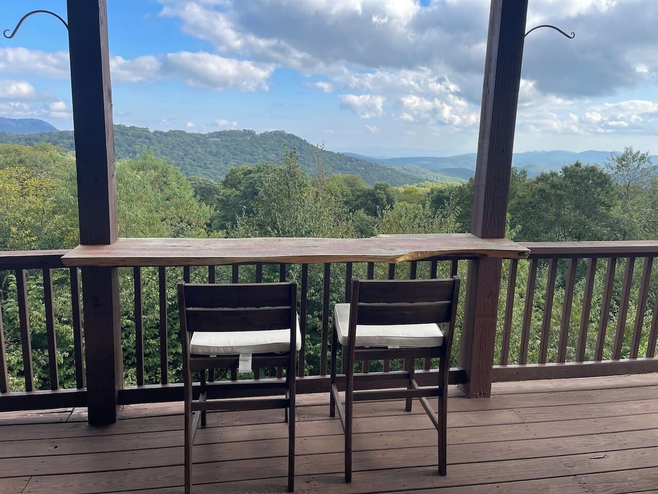 Une terrasse en bois avec deux chaises et une table, offrant une vue sur un paysage montagneux.