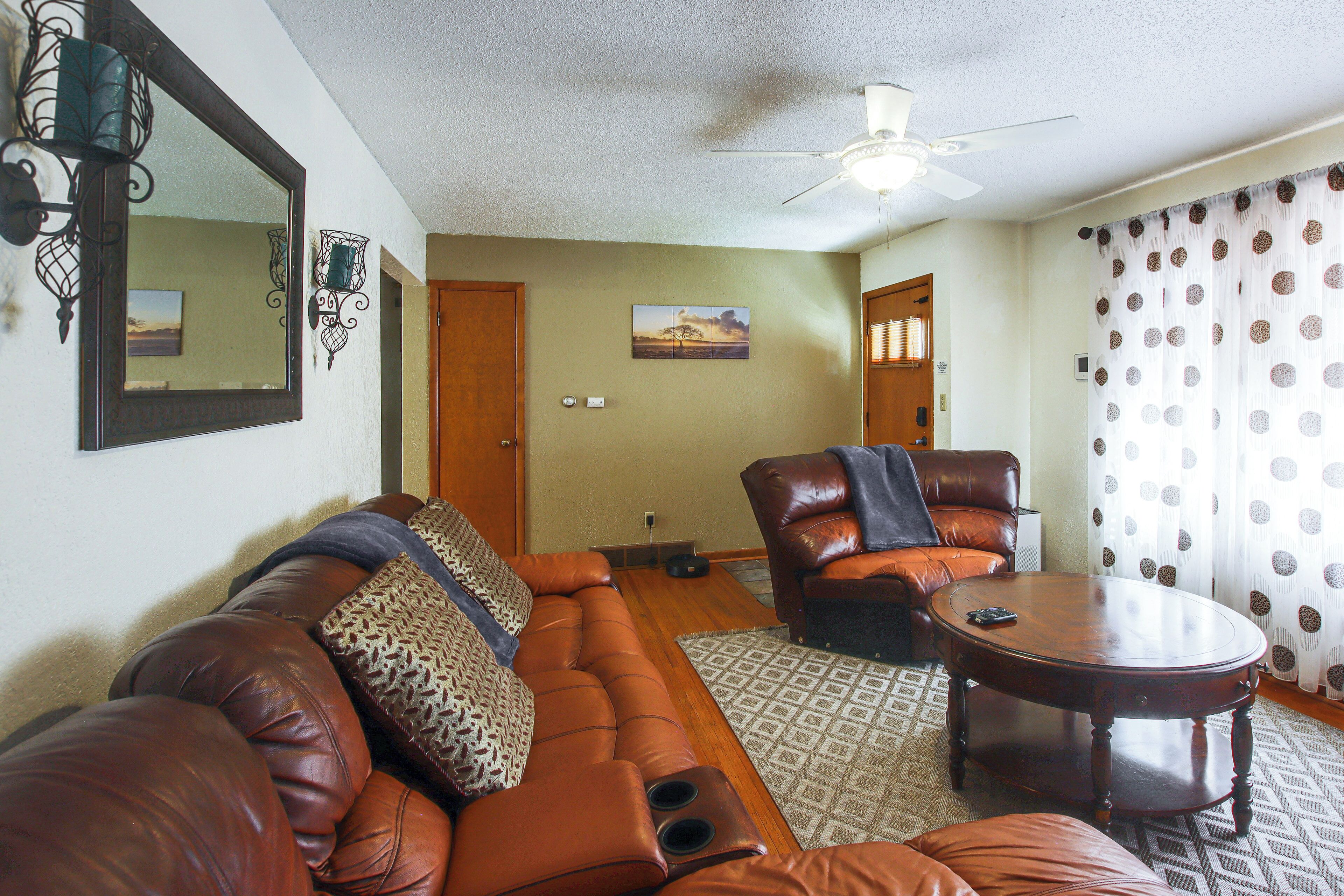 A living room with a brown leather sofa, a brown leather armchair, a wooden coffee table, and a ceiling fan.