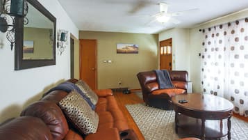 A living room with a brown leather sofa, a brown leather armchair, a wooden coffee table, and a ceiling fan.