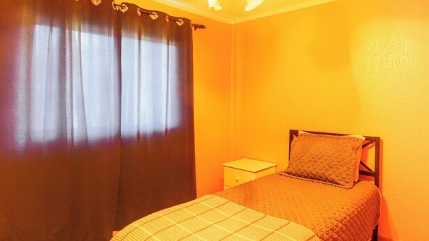 Une chambre à coucher comprenant un lit, une table de chevet, une fenêtre avec des rideaux et un mur orné d’un motif texturé.