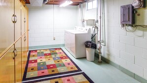 Une buanderie équipée d’un lave-linge, d’un sèche-linge, d’une poubelle et d’un tapis coloré.