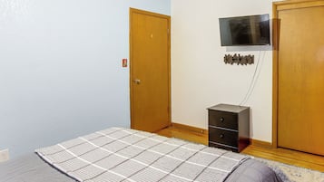 Un dormitorio con cama, cómoda, televisor montado en la pared y una puerta.