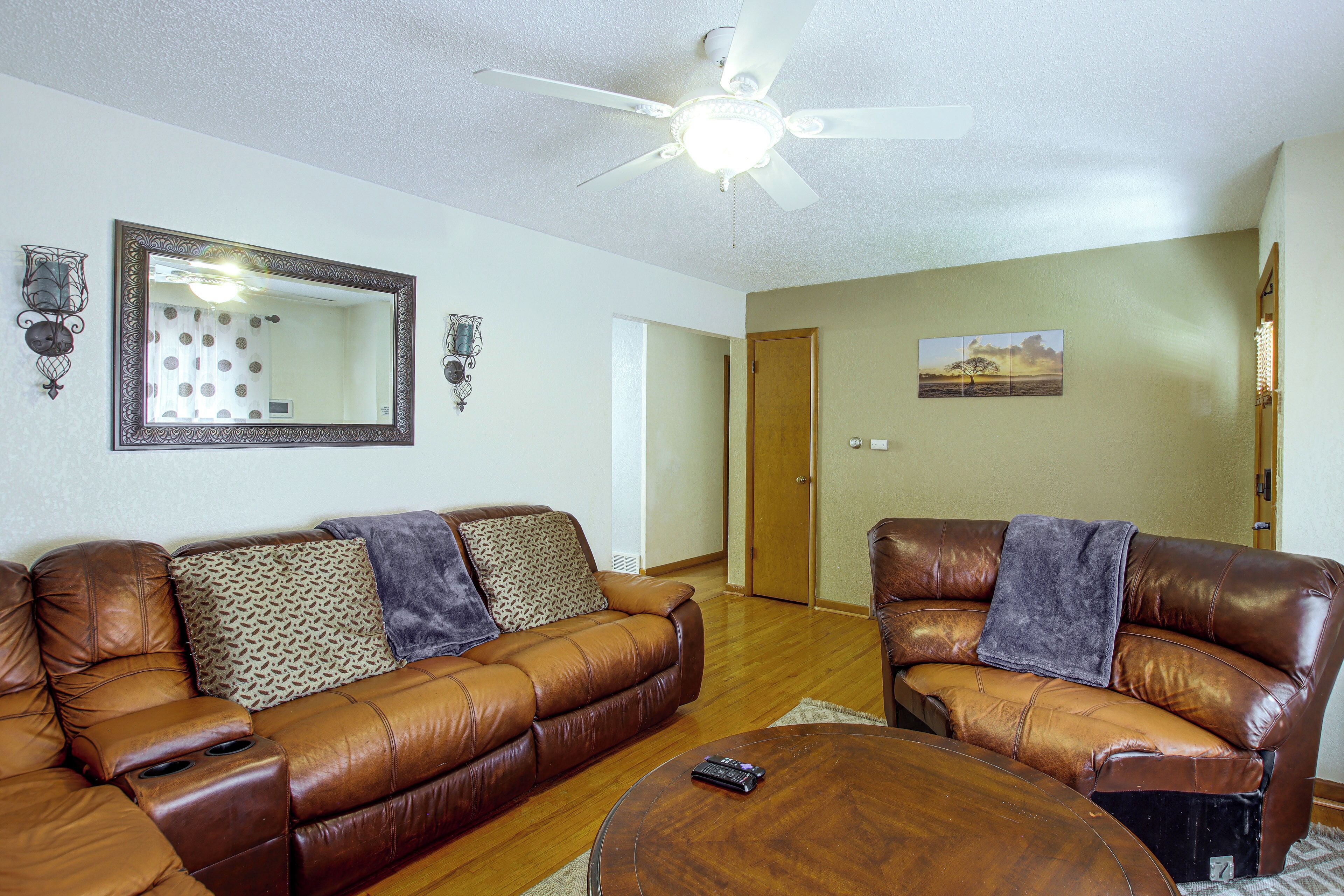 A living room with two brown leather sofas, a wooden coffee table, a ceiling fan, a large mirror, wall sconces, and a painting.