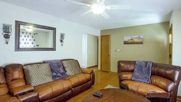 A living room with two brown leather sofas, a wooden coffee table, a ceiling fan, a large mirror, wall sconces, and a painting.