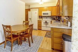 A compact kitchen with wooden cabinets, a microwave, a stove, and a dining area with a table and chairs. - Pet-friendly Waterloo Abode w/ Deck! (Waterloo)
