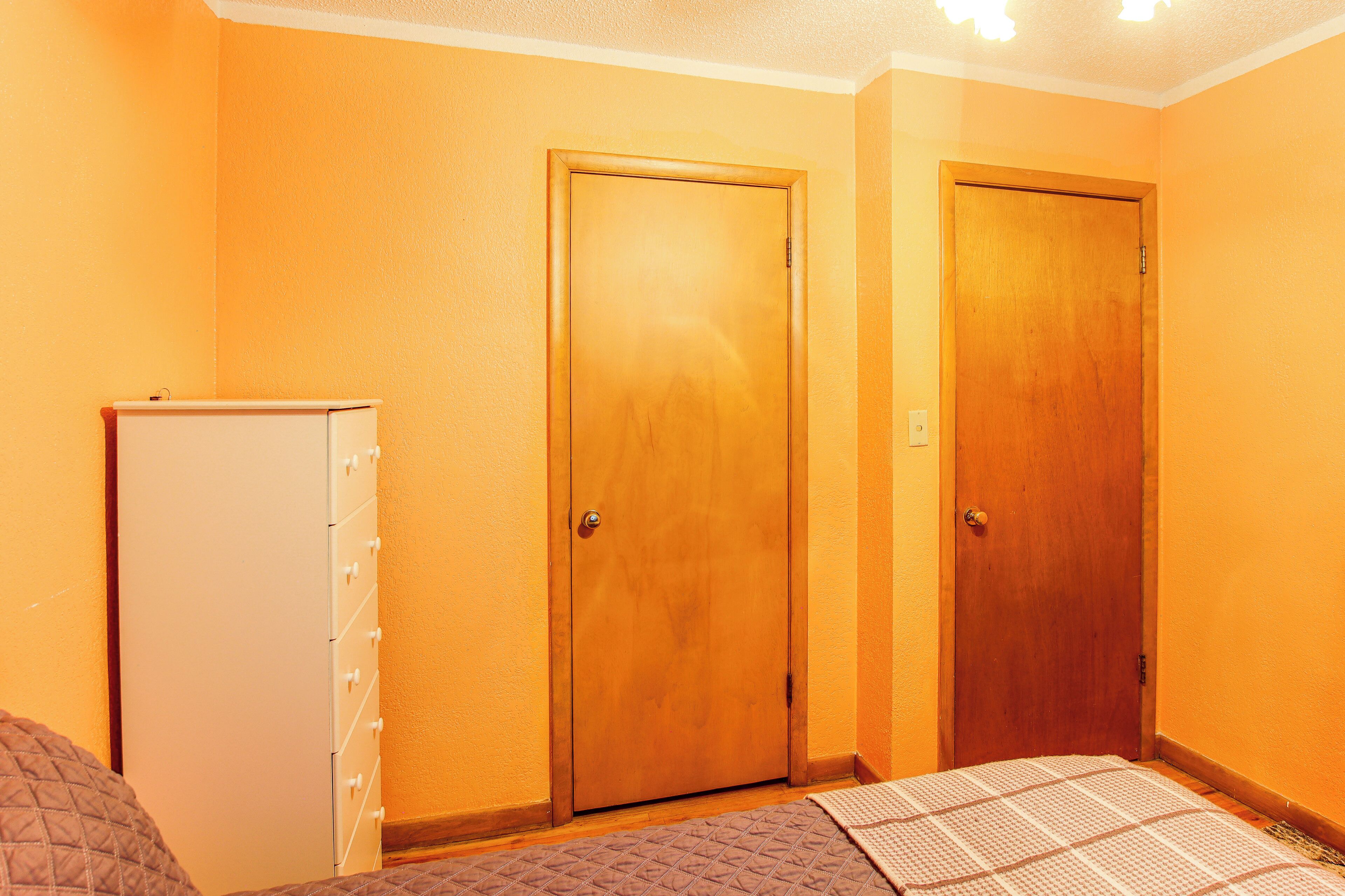 A room with two wooden doors, a white dresser, and a bed with a quilted cover.