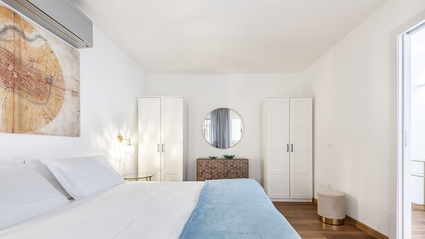 Une chambre avec un grand lit, une carte accrochée au mur, un miroir rond et une petite table sur laquelle est posée une plante.