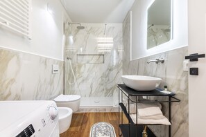 Ein modernes Badezimmer mit Toilette in Weiß, einem großen weißen Waschbecken, einer Duschkabine aus Glas und Holzboden.