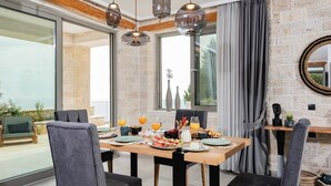 Uma sala de jantar com parede de pedra, janelas amplas e mesa posta para o café da manhã.