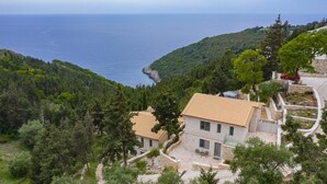Uma vila em estilo mediterrâneo com telhado em telhas, rodeada por vegetação densa e com vista para a costa.