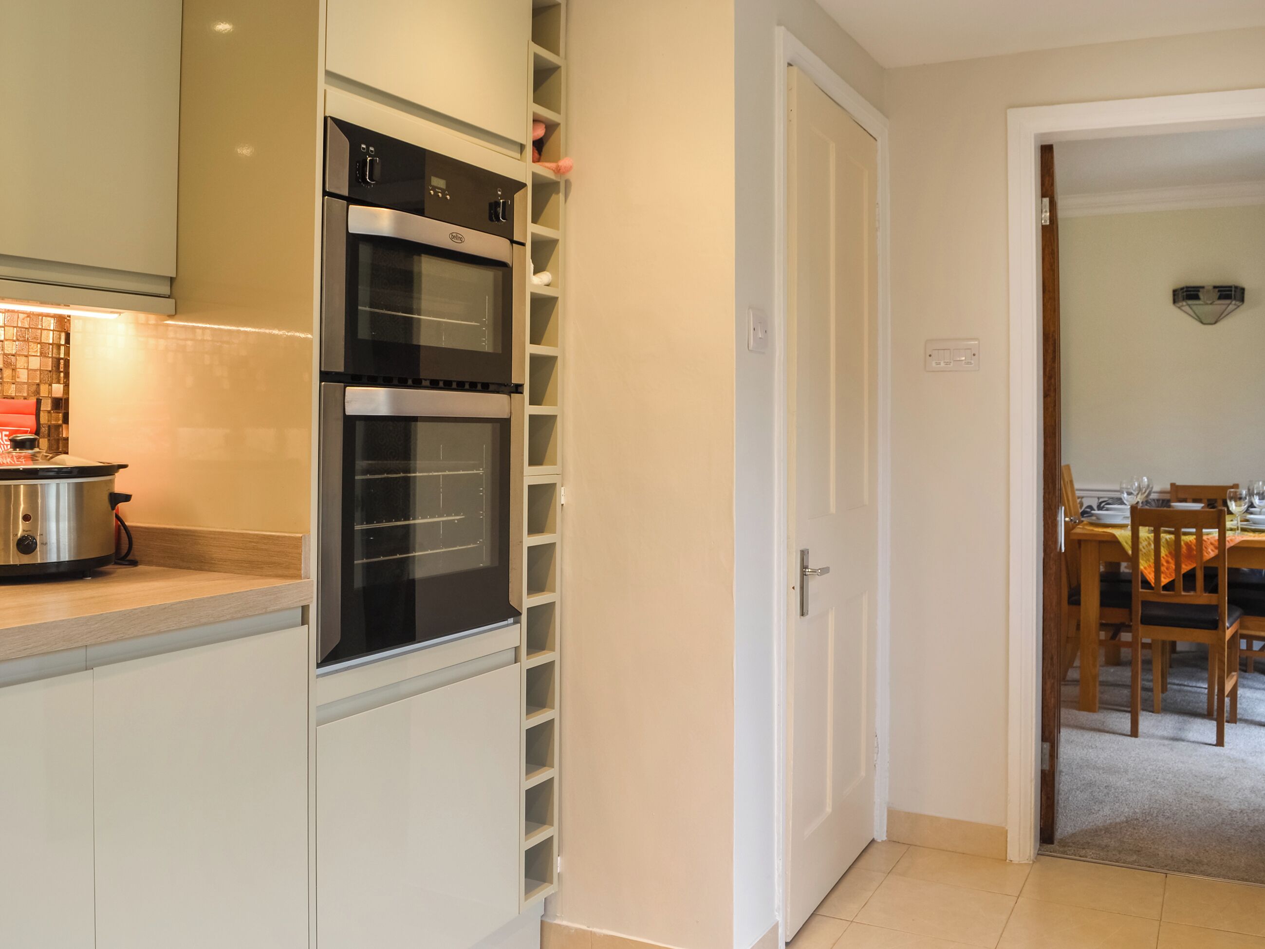 A modern kitchen with built-in appliances, a dining area with wooden furniture, and a tiled floor.