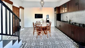 Un comedor con una mesa redonda y sillas, un dispensador de agua y una cocina con salpicadero estampado y armarios de madera.