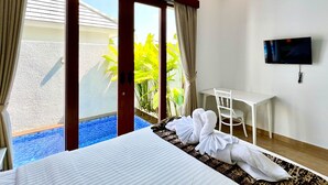 Habitación de hotel con cama, escritorio, televisor y vistas a una piscina y zonas verdes.