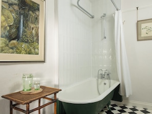 Une salle de bain avec une baignoire sur pieds de couleur verte, des murs recouverts de carreaux blancs, un tableau encadré et un sol à carreaux.