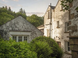 A rustic stone building with a pitched roof, a window with shutters, and a visible chimney.