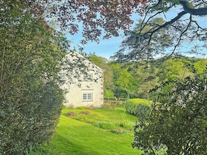 Une maison en pierre avec une fenêtre, entourée d’une végétation luxuriante et d’une pelouse bien entretenue.