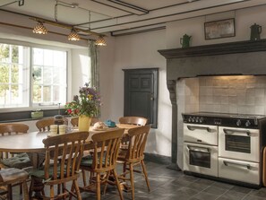 A kitchen with a dining table, chairs, a stove, and a window with curtains.