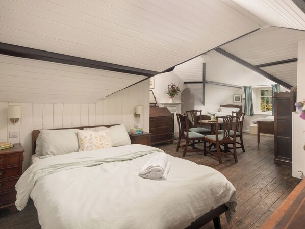 Une chambre à coucher avec un grand lit, une commode en bois, une petite table avec des chaises et une fenêtre avec des rideaux.