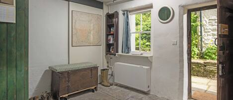 A room with a radiator, a window with a view of greenery, a wooden cabinet with boots, and a map on the wall.