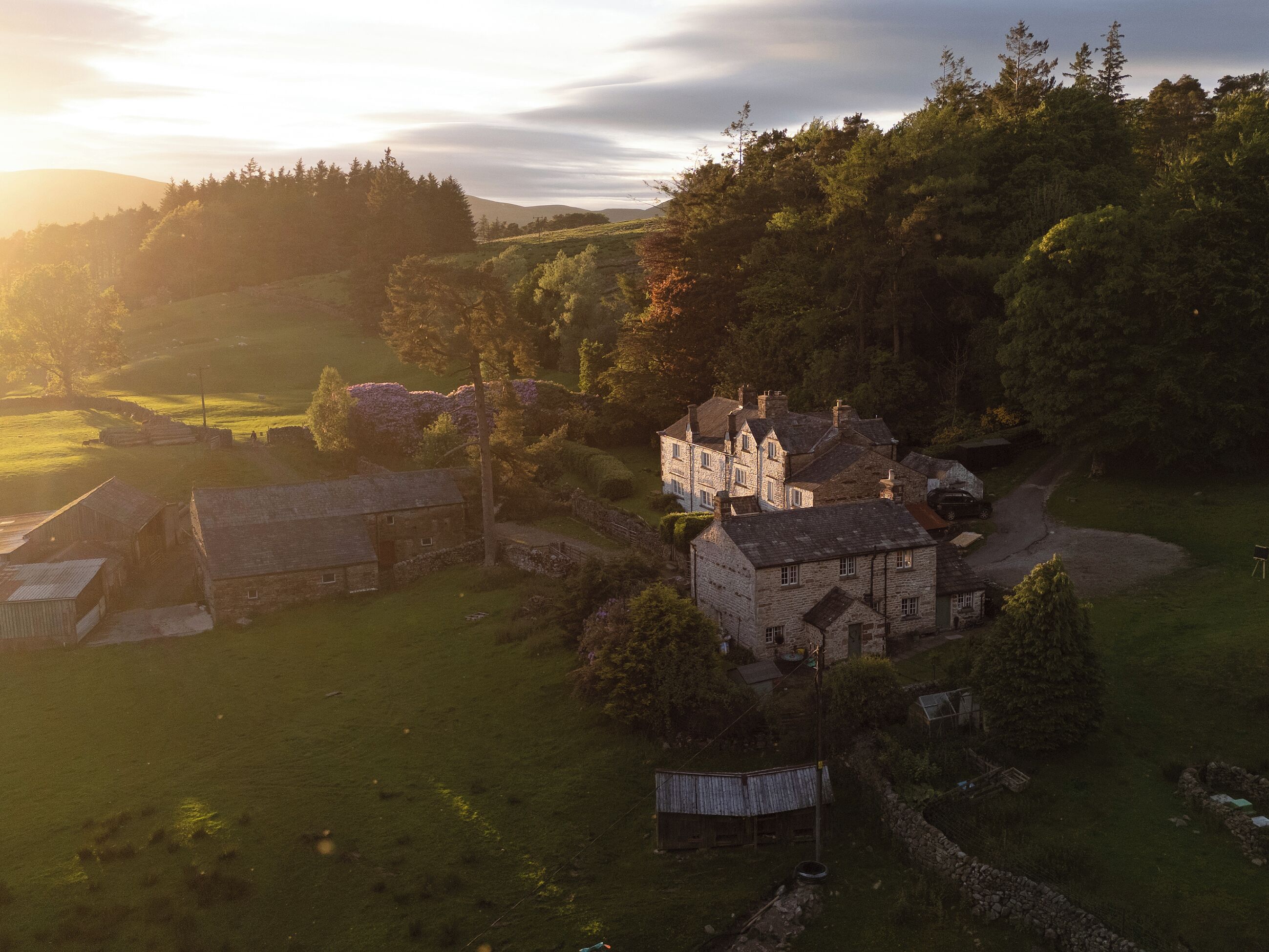 A rural landscape with stone buildings, a large house with multiple chimneys, and surrounding greenery.