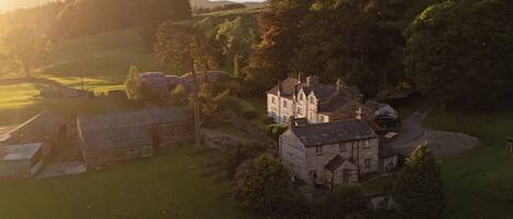 A rural landscape with stone buildings, a large house with multiple chimneys, and surrounding greenery.