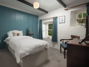 Un dormitorio con una cama, una silla, un ventanal con cortinas, una lámpara y un cuadro en la pared.