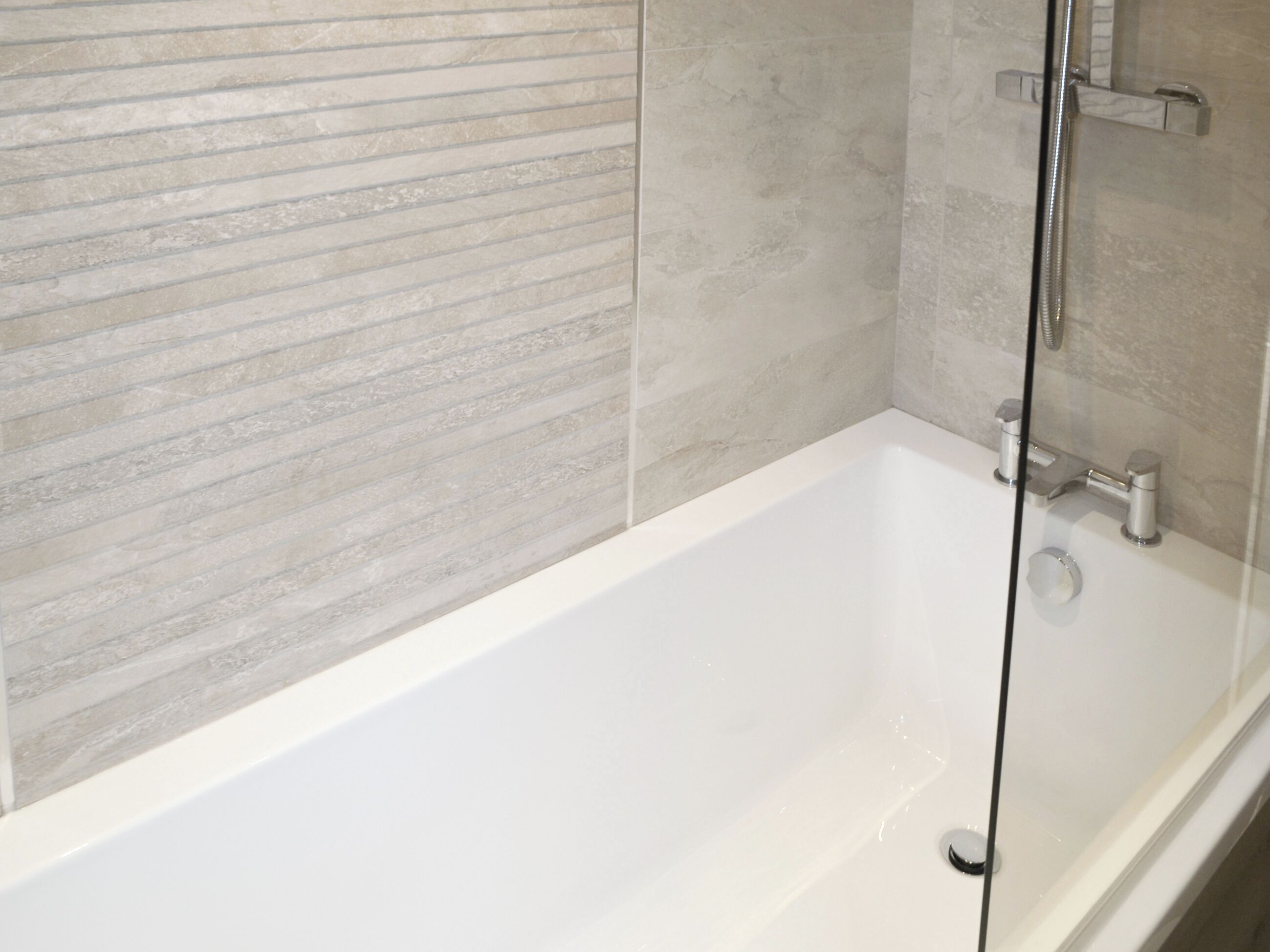 A modern bathroom with a white bathtub, a glass shower enclosure, and a textured wall.