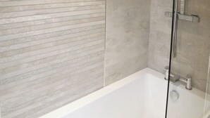Un baño moderno con una bañera blanca, cerramiento de ducha de vidrio y pared con textura.