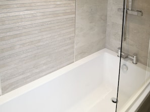 Un baño moderno con una bañera blanca, cerramiento de ducha de vidrio y pared con textura.