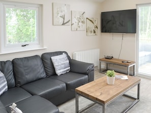 A modern living room with a black leather sofa, a wooden coffee table, and a flat-screen TV mounted on the wall.