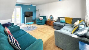 Un salon avec des canapés de couleur turquoise et grise, un téléviseur et une petite table ronde.