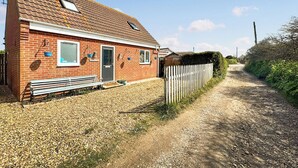 Une maison en briques avec une allée en gravier, une clôture en bois et un banc.